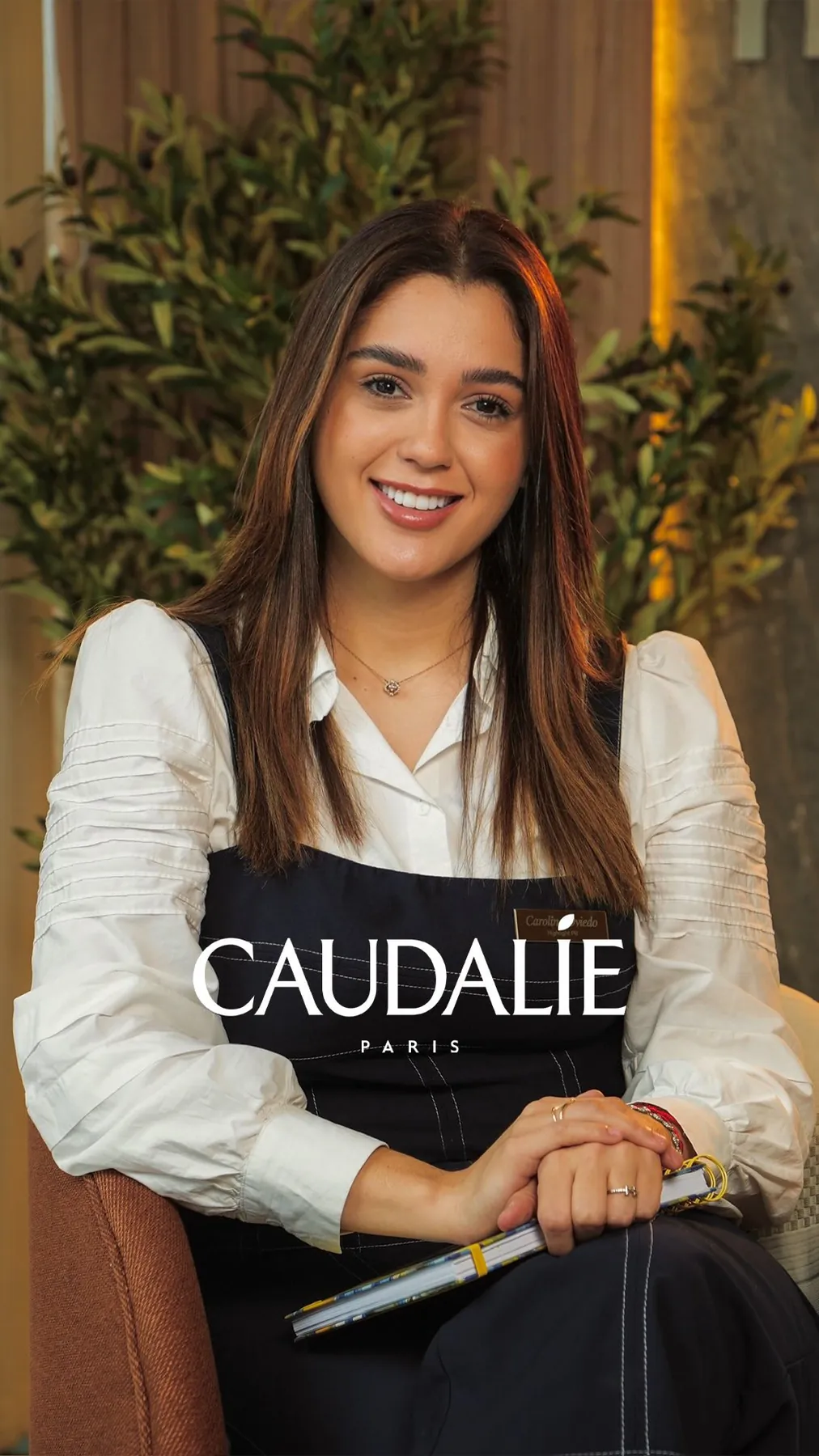 Anfitriona de Caudalie sonríe en un showroom cálido con plantas.