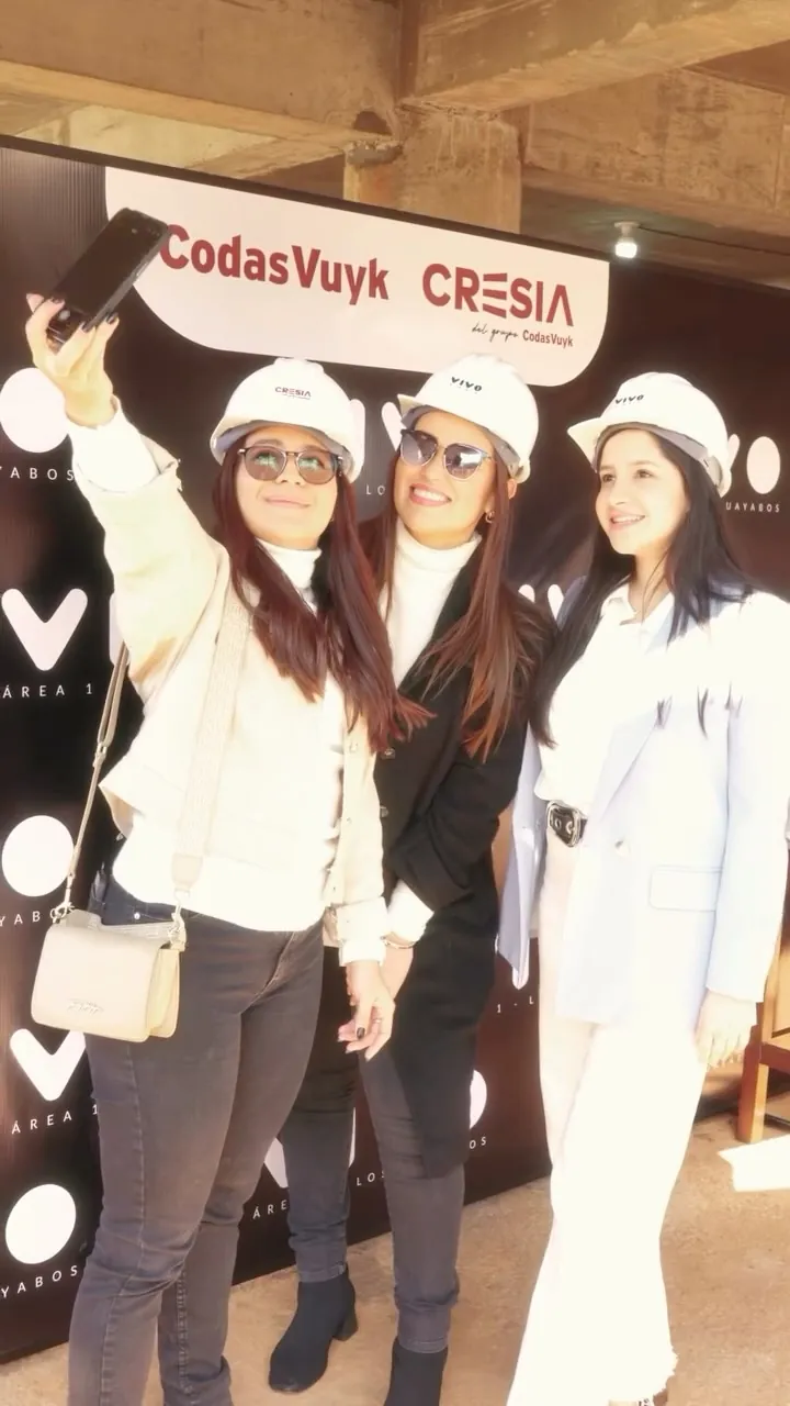 Tres invitadas con cascos blancos se toman una selfie frente al cartel de Codas Vuyk y Cresia.
