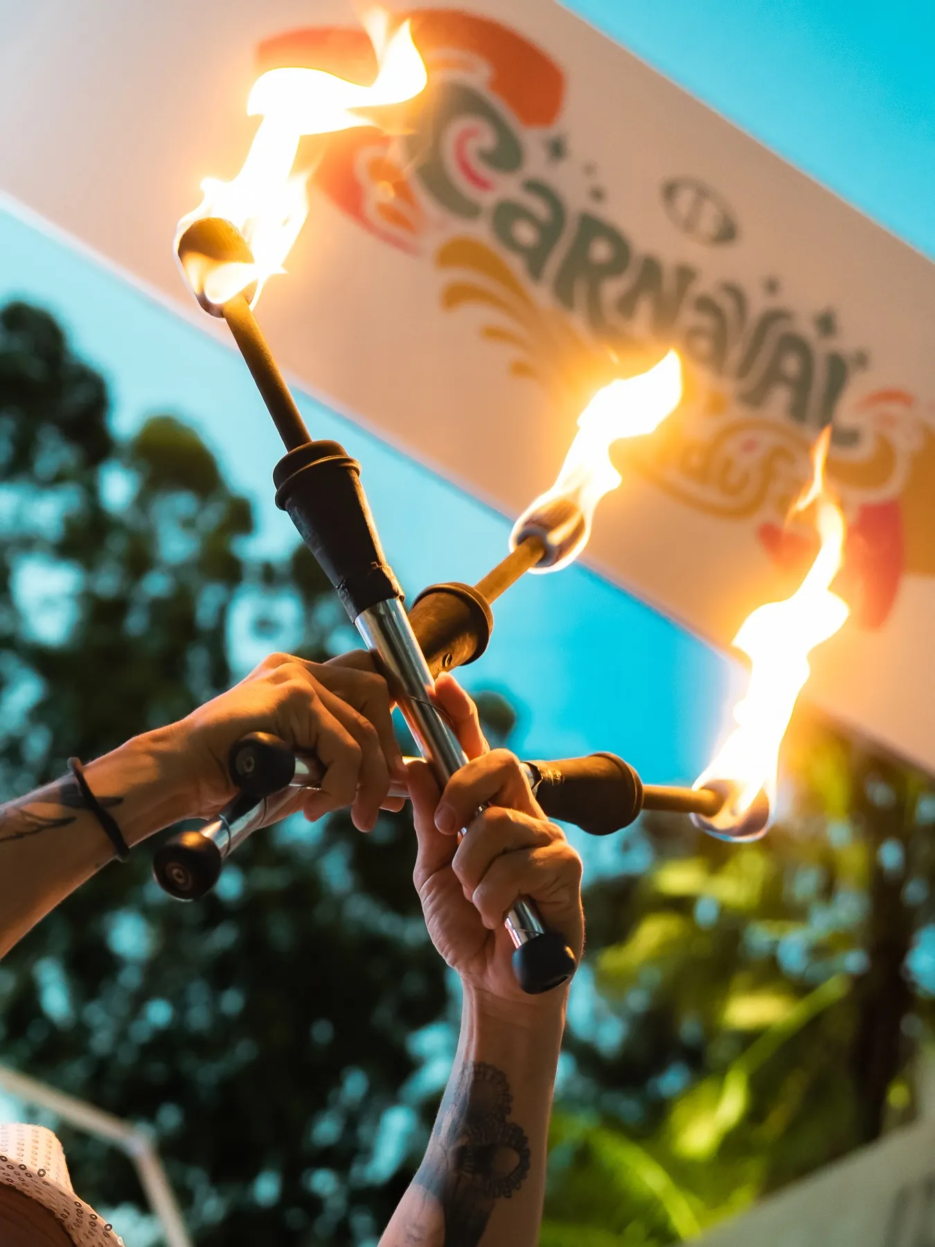 Malabarista con antorchas encendidas frente a un cartel de Carnaval de Indufar.