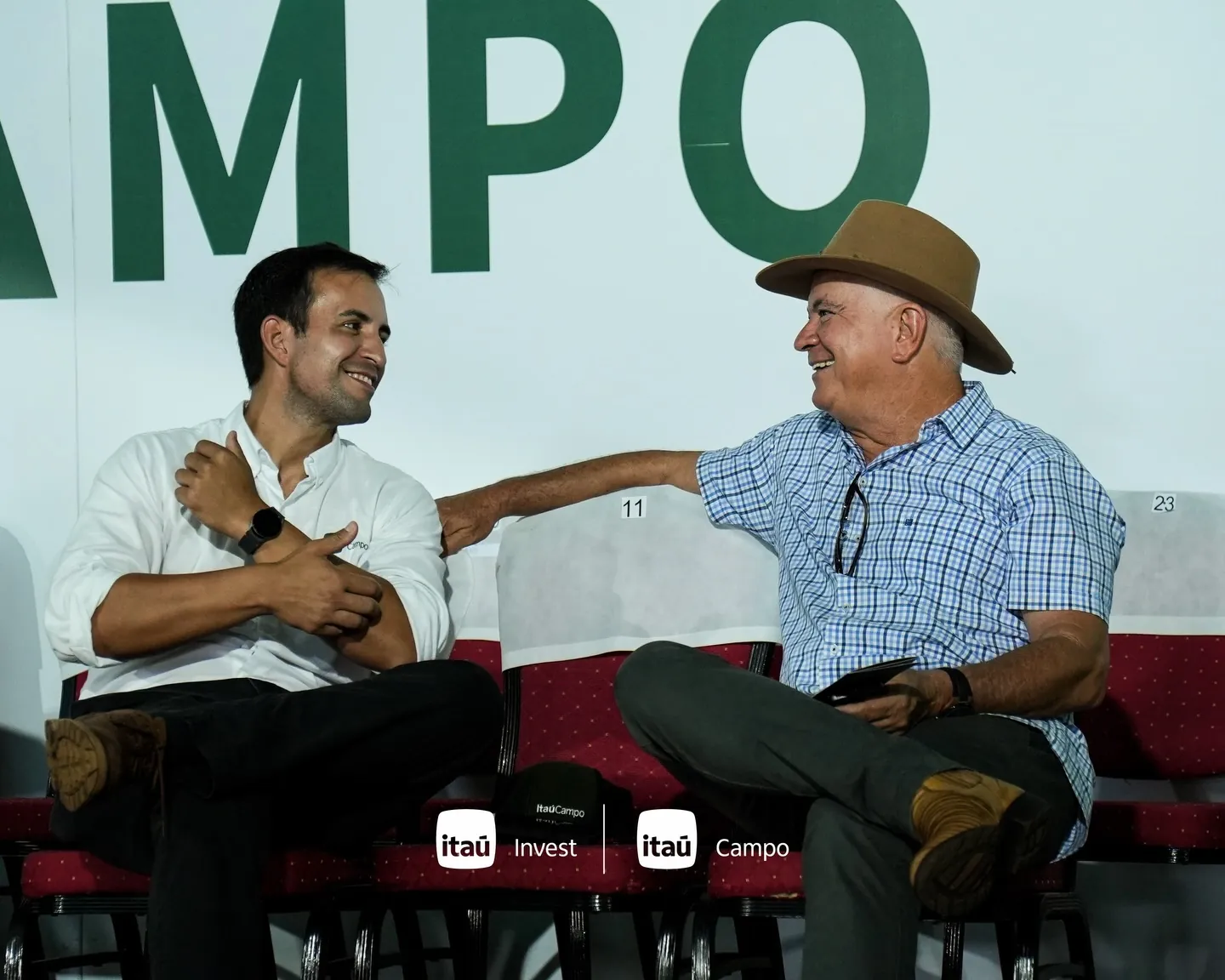 Dos invitados conversan y ríen frente al cartel de Itaú Campo.